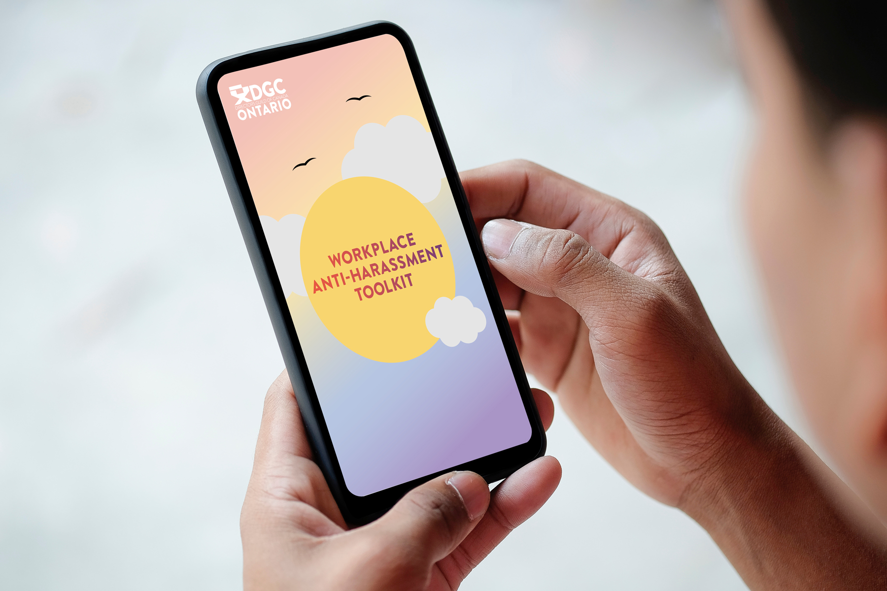 Person holding a phone with the title image of the DCG Ontario harassment toolkit on it. Designed by Jen Spinner.