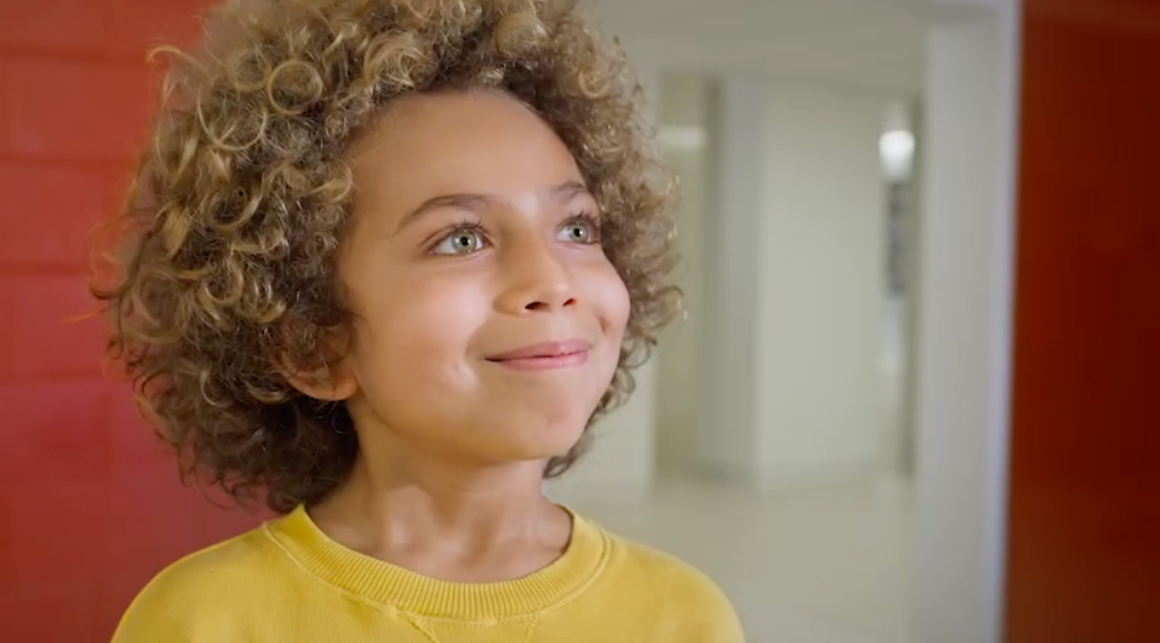 Aramark commerical screengrab art directed by Jen Spinner. Image of a young boy with curly hair and cinammon skin smiling with mouth closed.