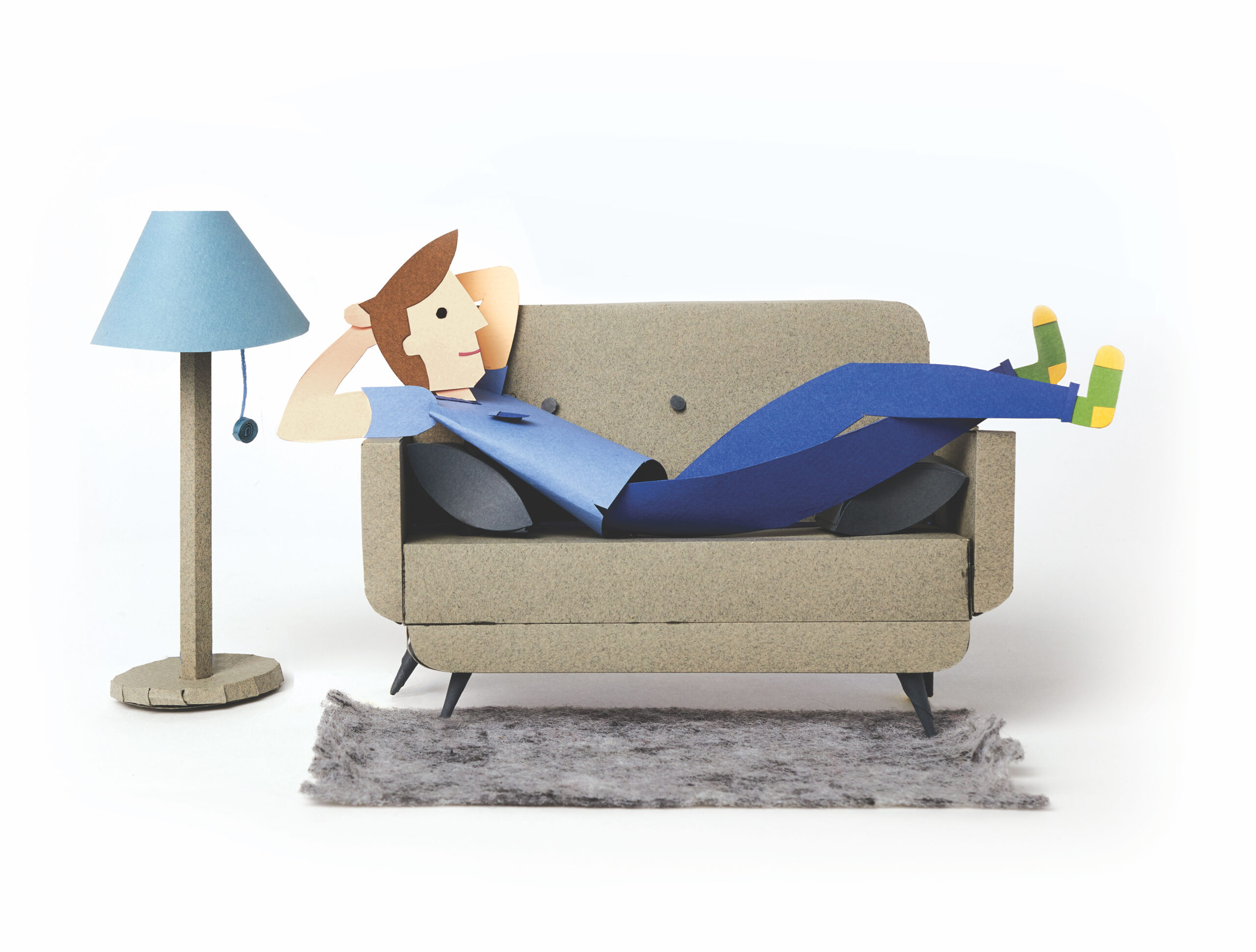 paper sculpture of laying on the couch with a paper sculpture floor lamp beside him