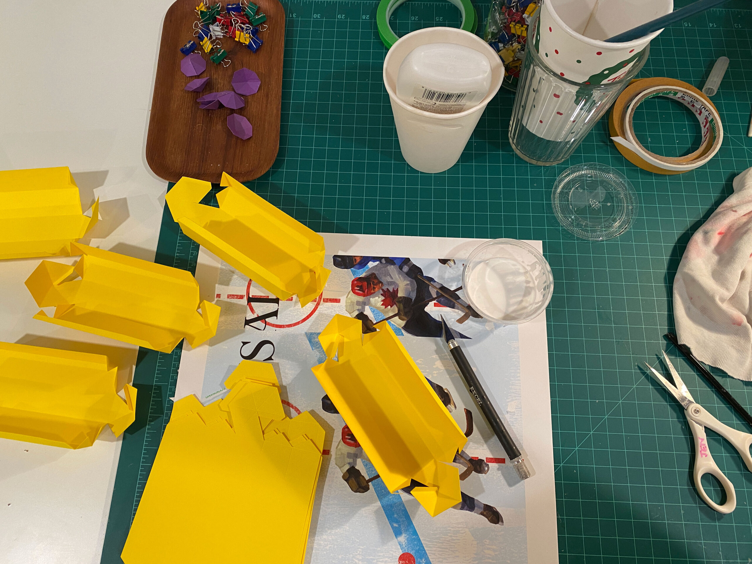 A messy desk full of materials used to create yellow geometric paper sculptures by Jen Spinner.